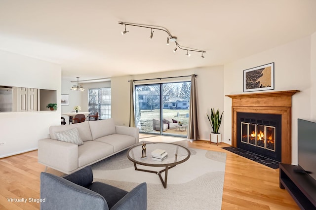 living area featuring light wood-type flooring, an inviting chandelier, a fireplace with flush hearth, and rail lighting