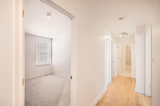 hallway featuring light wood finished floors and baseboards