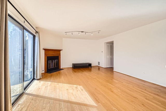 unfurnished living room with light wood finished floors, a fireplace with flush hearth, visible vents, and rail lighting