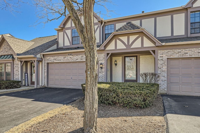 view of front facade featuring brick siding, stucco siding, a shingled roof, a garage, and driveway