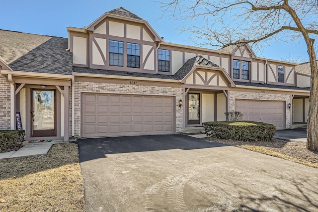 tudor home with a garage, brick siding, driveway, roof with shingles, and stucco siding