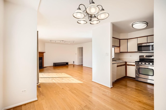 kitchen with light wood finished floors, open floor plan, stainless steel appliances, light countertops, and a chandelier