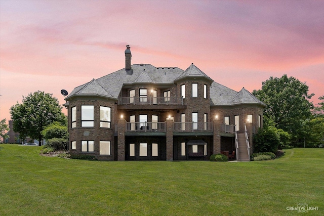 rear view of house with a yard, brick siding, a chimney, and a balcony