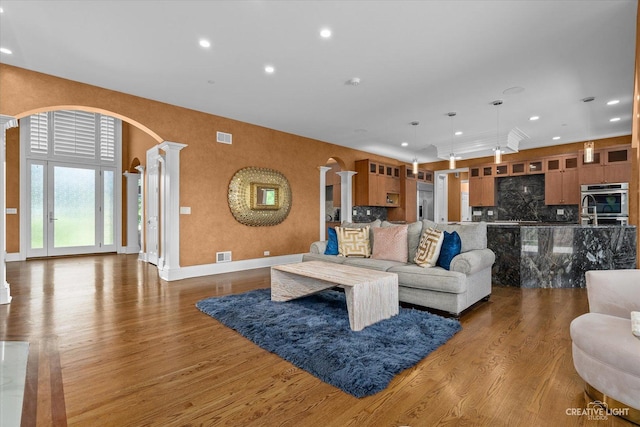 living area with arched walkways, visible vents, wood finished floors, and decorative columns