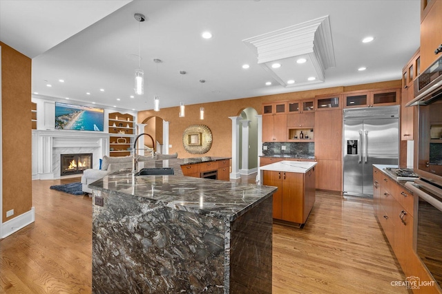 kitchen with arched walkways, a spacious island, a high end fireplace, appliances with stainless steel finishes, and brown cabinetry