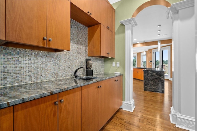 kitchen with decorative columns, light wood finished floors, tasteful backsplash, a sink, and dark stone countertops