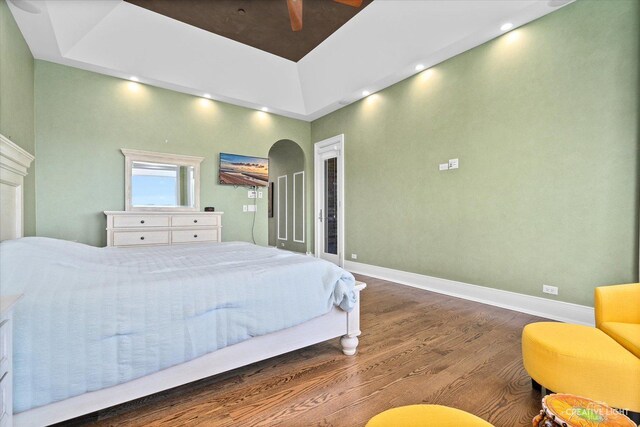 bedroom with arched walkways, recessed lighting, a raised ceiling, wood finished floors, and baseboards