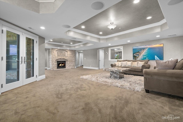 carpeted living area with a large fireplace, visible vents, baseboards, ornamental molding, and a tray ceiling