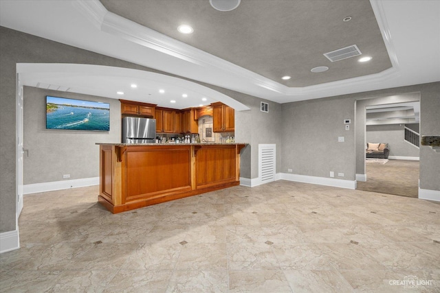 kitchen featuring arched walkways, a tray ceiling, visible vents, brown cabinetry, and freestanding refrigerator