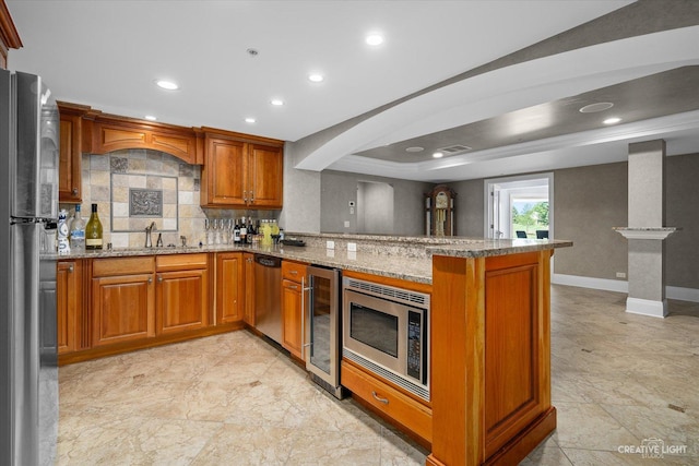 kitchen featuring beverage cooler, a peninsula, a sink, appliances with stainless steel finishes, and brown cabinetry