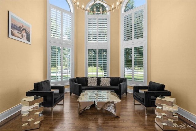 living room featuring a towering ceiling, baseboards, a chandelier, and wood finished floors