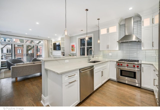 kitchen with a peninsula, a sink, open floor plan, appliances with stainless steel finishes, and wall chimney exhaust hood