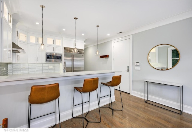 kitchen with white cabinets, glass insert cabinets, built in appliances, a peninsula, and extractor fan