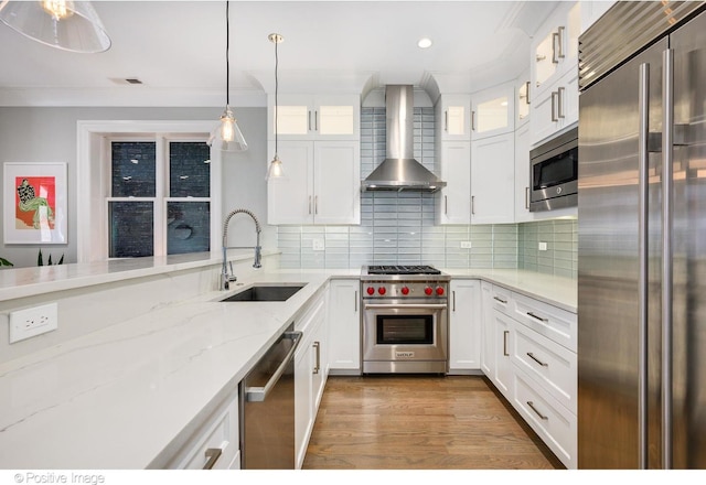 kitchen featuring premium appliances, glass insert cabinets, white cabinets, a sink, and wall chimney exhaust hood