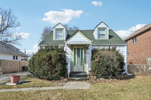 cape cod-style house with a shingled roof, a front lawn, and fence