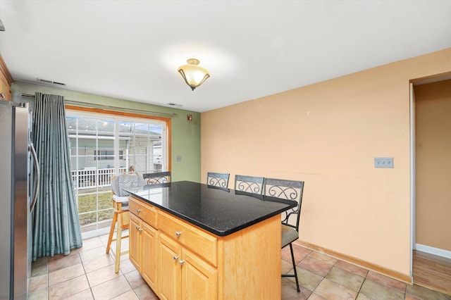 kitchen featuring baseboards, visible vents, freestanding refrigerator, a kitchen bar, and a center island