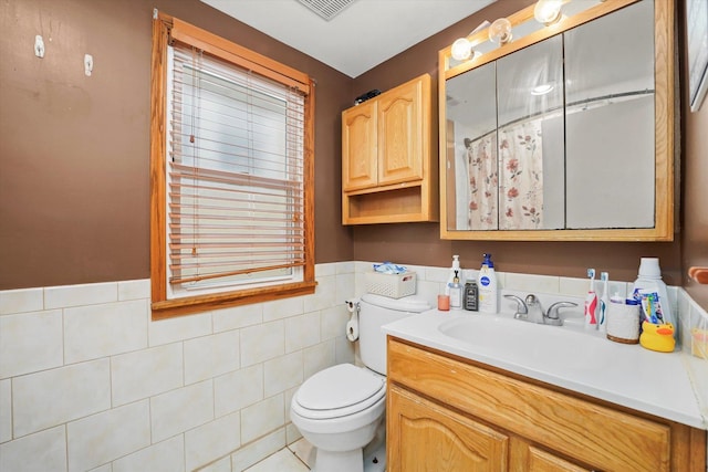 bathroom with vanity, visible vents, wainscoting, tile walls, and toilet