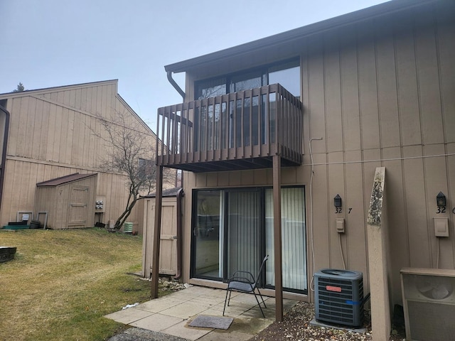 rear view of house with central AC unit, a balcony, a yard, a storage unit, and an outdoor structure