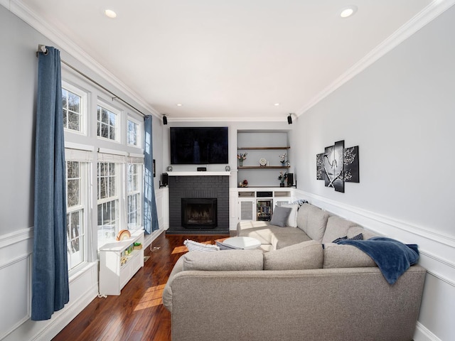 living area with a wainscoted wall, a brick fireplace, dark wood-style flooring, and crown molding