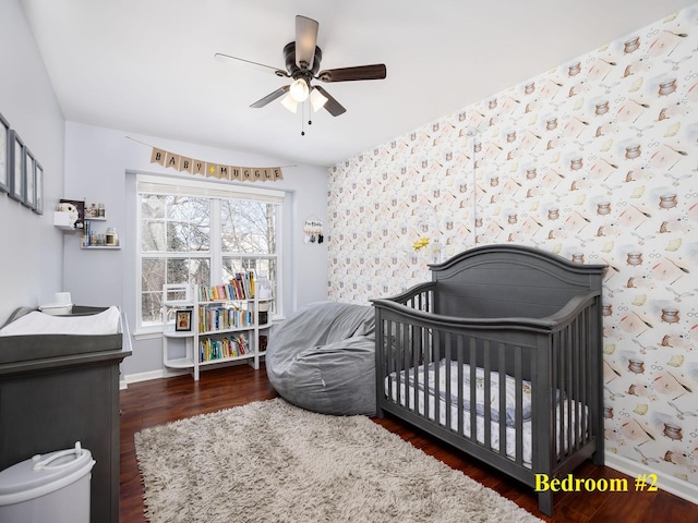 bedroom featuring ceiling fan, a crib, wood finished floors, and baseboards