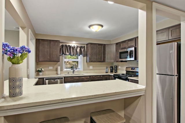 kitchen with light stone counters, a breakfast bar area, stainless steel appliances, a sink, and dark brown cabinets