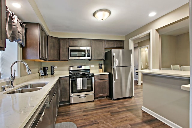 kitchen with light stone counters, a sink, dark brown cabinets, appliances with stainless steel finishes, and dark wood finished floors