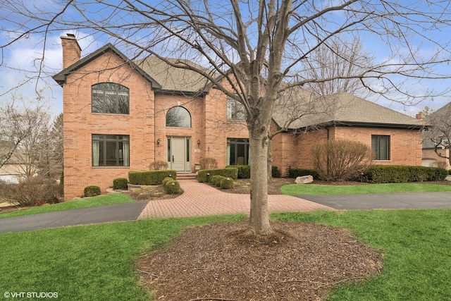 traditional-style home featuring a chimney, brick siding, and a front yard