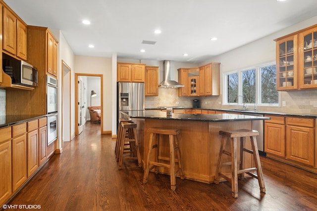 kitchen with dark wood-style floors, wall chimney range hood, a kitchen breakfast bar, and appliances with stainless steel finishes