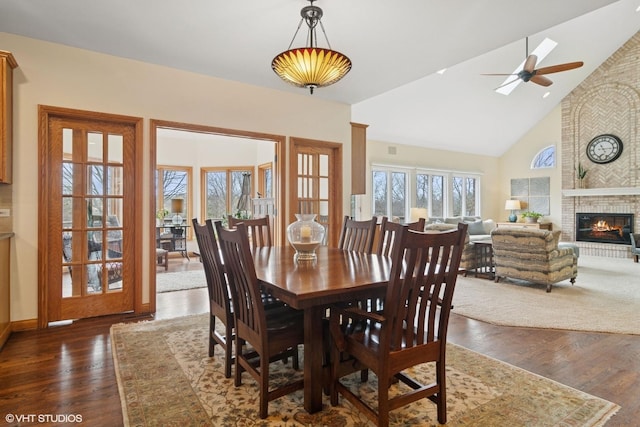 dining space with high vaulted ceiling, ceiling fan, dark wood-type flooring, and a brick fireplace