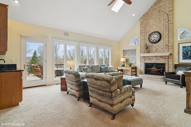 living area with ceiling fan, a wealth of natural light, a brick fireplace, and light carpet