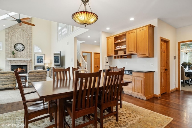 dining space featuring dark wood-style flooring, stairs, a fireplace, recessed lighting, and a ceiling fan