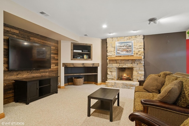 living area featuring a stone fireplace, baseboards, light colored carpet, and visible vents