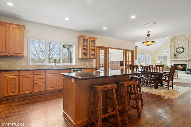 kitchen featuring a sink, a kitchen breakfast bar, glass insert cabinets, open floor plan, and dark countertops