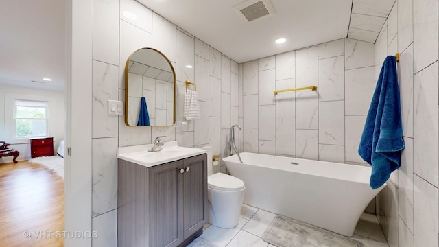 bathroom featuring a freestanding tub, recessed lighting, visible vents, vanity, and tile walls