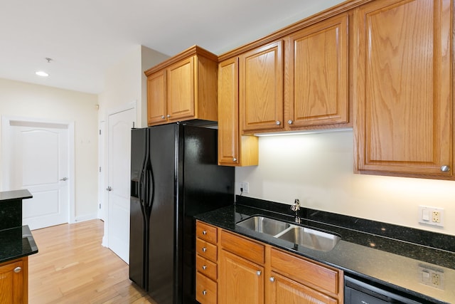 kitchen with light wood-style flooring, a sink, dark stone counters, dishwasher, and black fridge