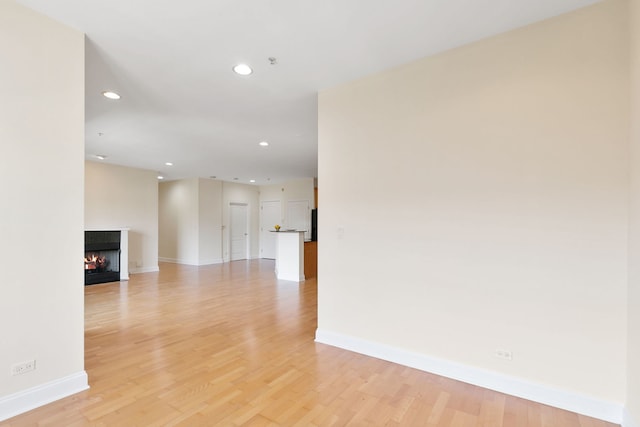 empty room featuring recessed lighting, baseboards, light wood-style flooring, and a multi sided fireplace