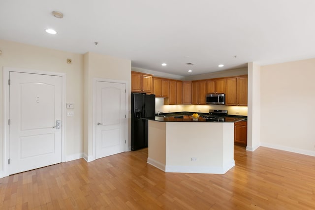 kitchen with dark countertops, a kitchen island, stainless steel appliances, light wood-type flooring, and recessed lighting