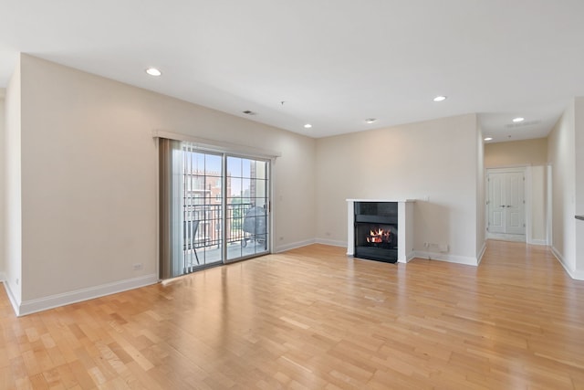 unfurnished living room featuring light wood-type flooring, a fireplace with flush hearth, baseboards, and recessed lighting