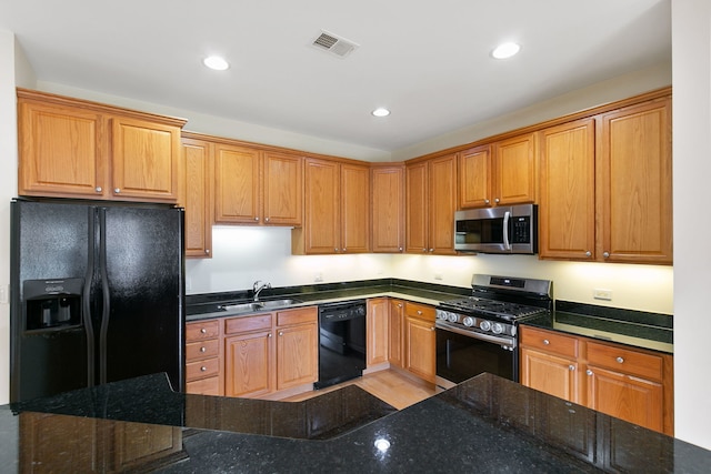 kitchen featuring black appliances, dark stone countertops, a sink, and visible vents