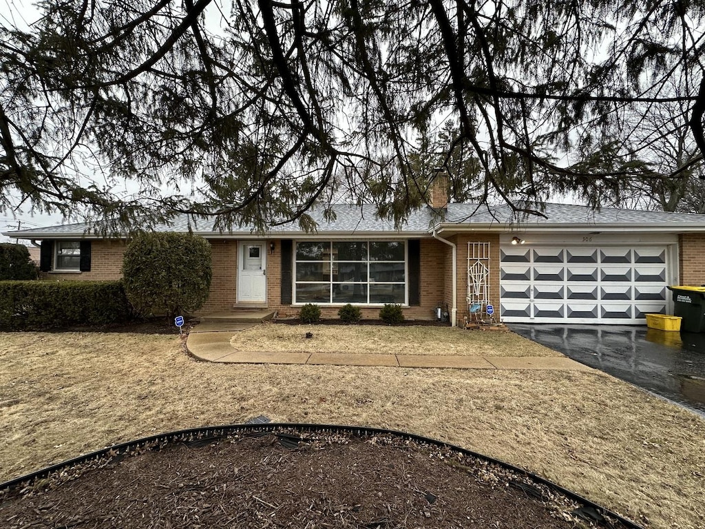 view of front facade with brick siding, driveway, a chimney, and an attached garage