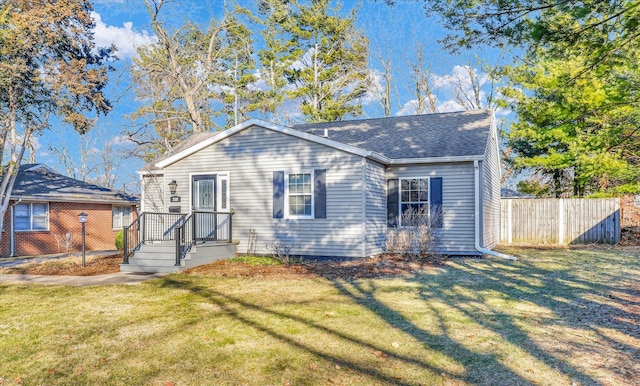 view of front of home with a front yard, fence, and roof with shingles