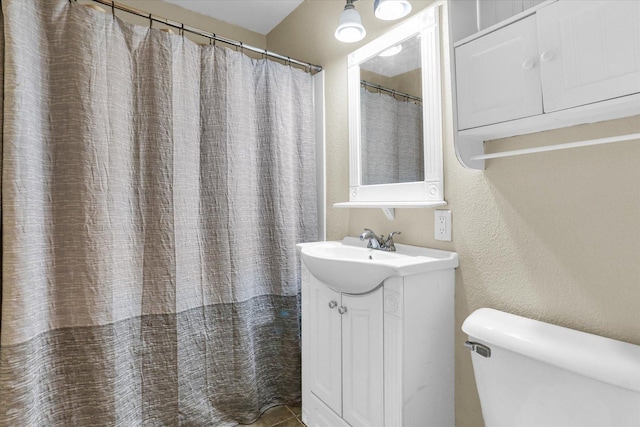 bathroom featuring toilet, vanity, and a textured wall