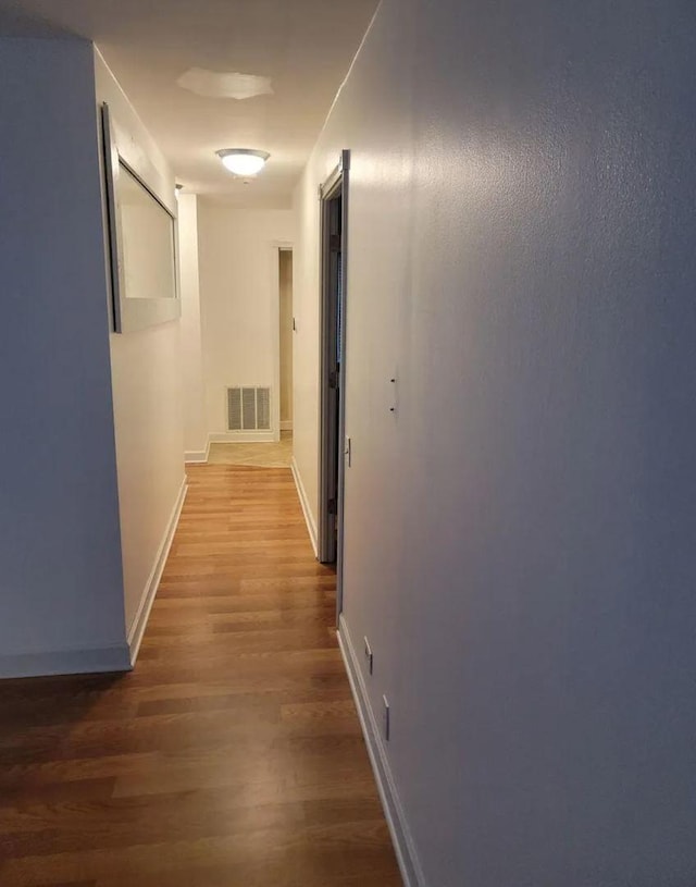 hall with visible vents, baseboards, and wood finished floors