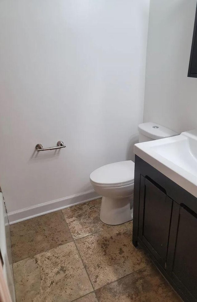 bathroom featuring toilet, stone finish floor, baseboards, and vanity