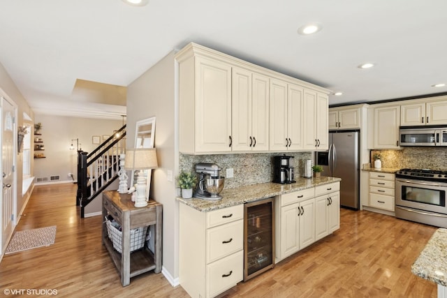 kitchen featuring beverage cooler, stainless steel appliances, light wood-type flooring, decorative backsplash, and light stone countertops