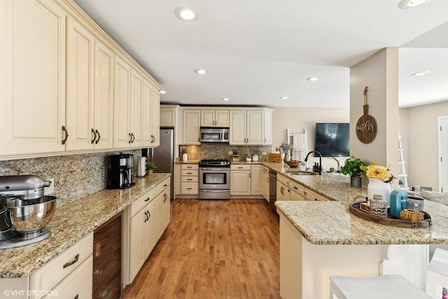 kitchen with decorative backsplash, a peninsula, cream cabinets, stainless steel appliances, and a kitchen bar