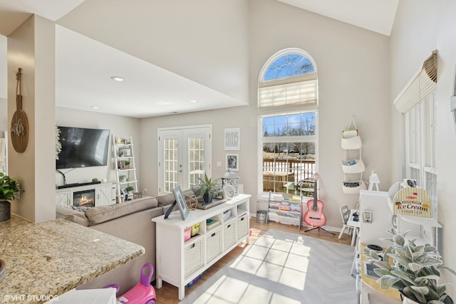 playroom featuring high vaulted ceiling, recessed lighting, french doors, light wood-type flooring, and a glass covered fireplace