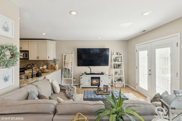 living room with french doors, a glass covered fireplace, light wood-style flooring, and recessed lighting