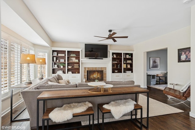 living area featuring dark wood-style floors, a brick fireplace, baseboards, and ceiling fan