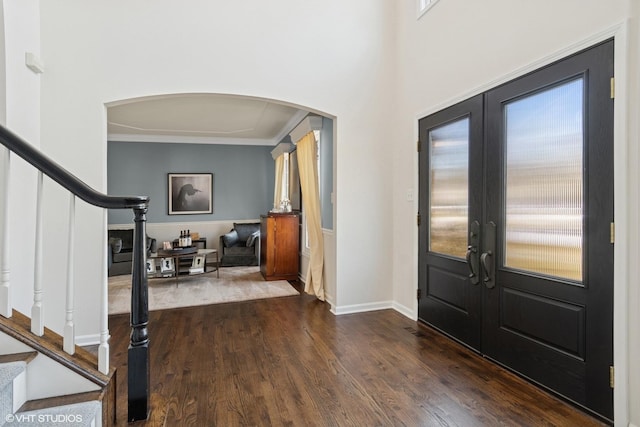 foyer entrance with stairway, baseboards, arched walkways, dark wood-type flooring, and french doors